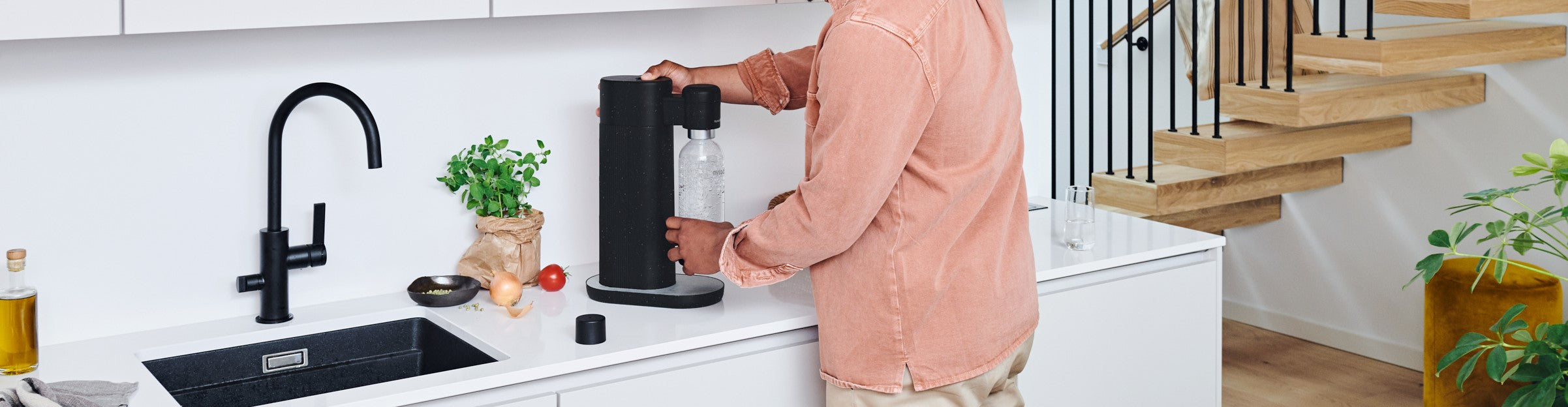 A man using a black Mysoda Toby sparkling water maker in a white kitchen