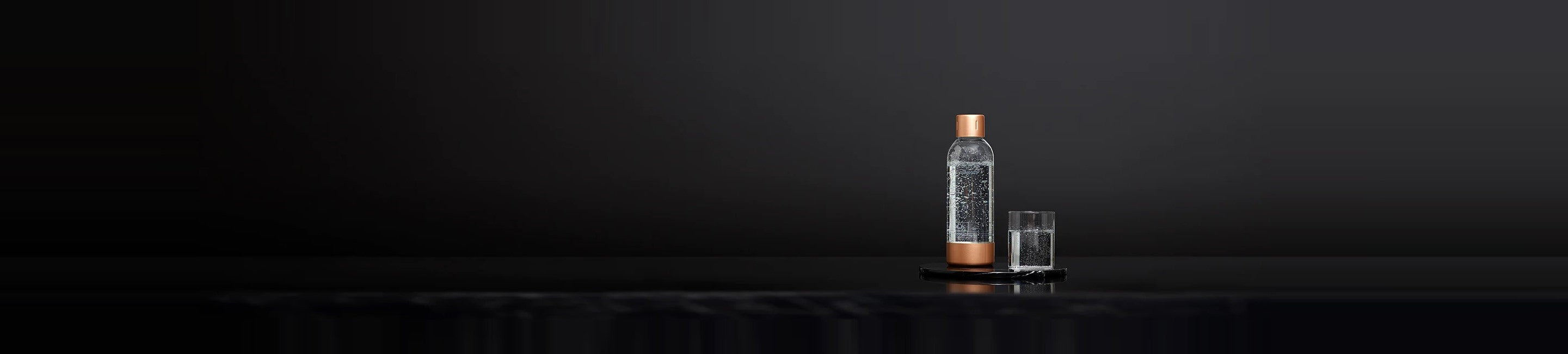 A Mysoda water bottle with copper lid and bottom and a glass of sparkling water in front of a black background
