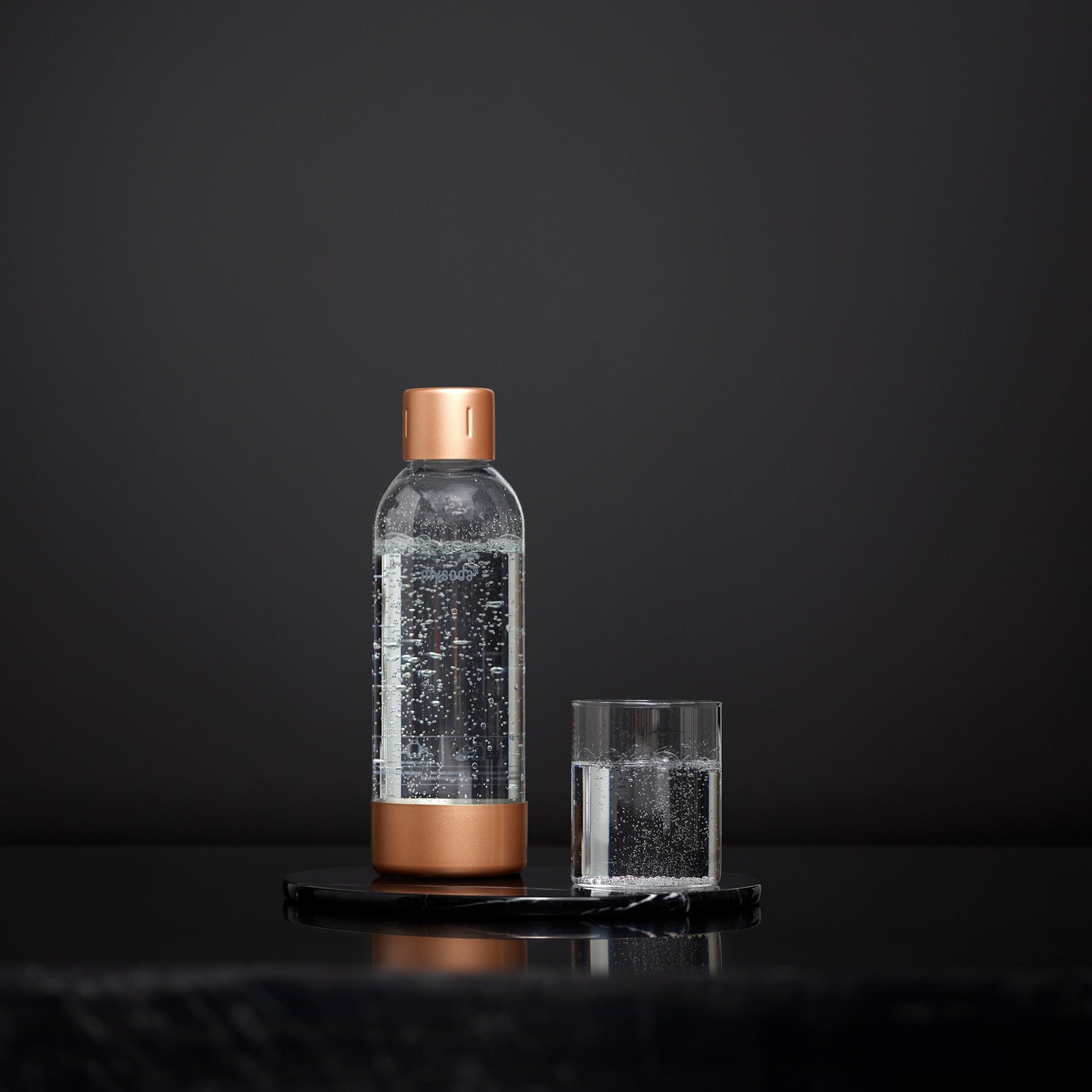 A copper Mysoda premium bottle and a glass of water in front of black background #väri_copper