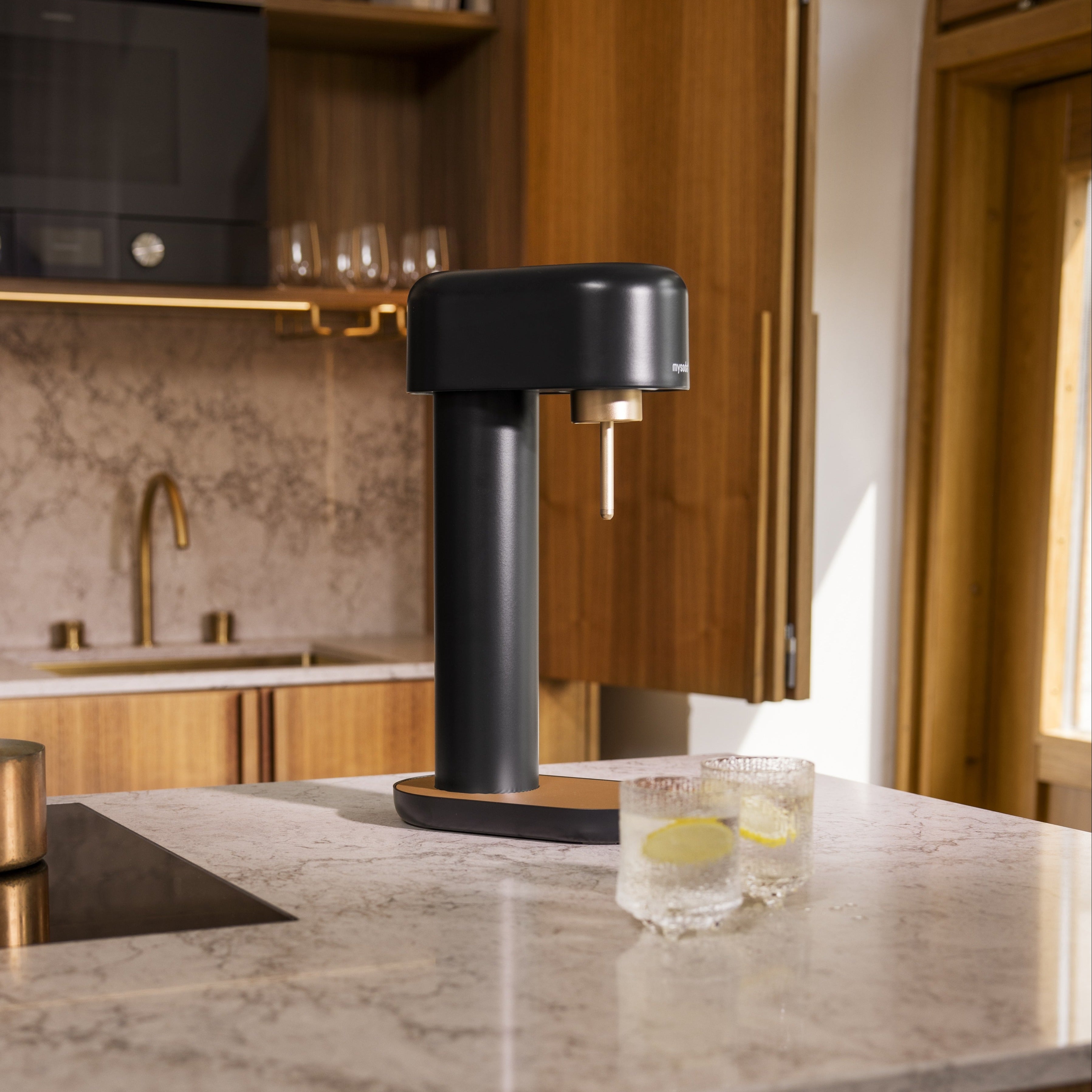 A black and copper Ruby 2 soda maker on a marble kitchen counter in front of wooden kitchen cupboards with copper details