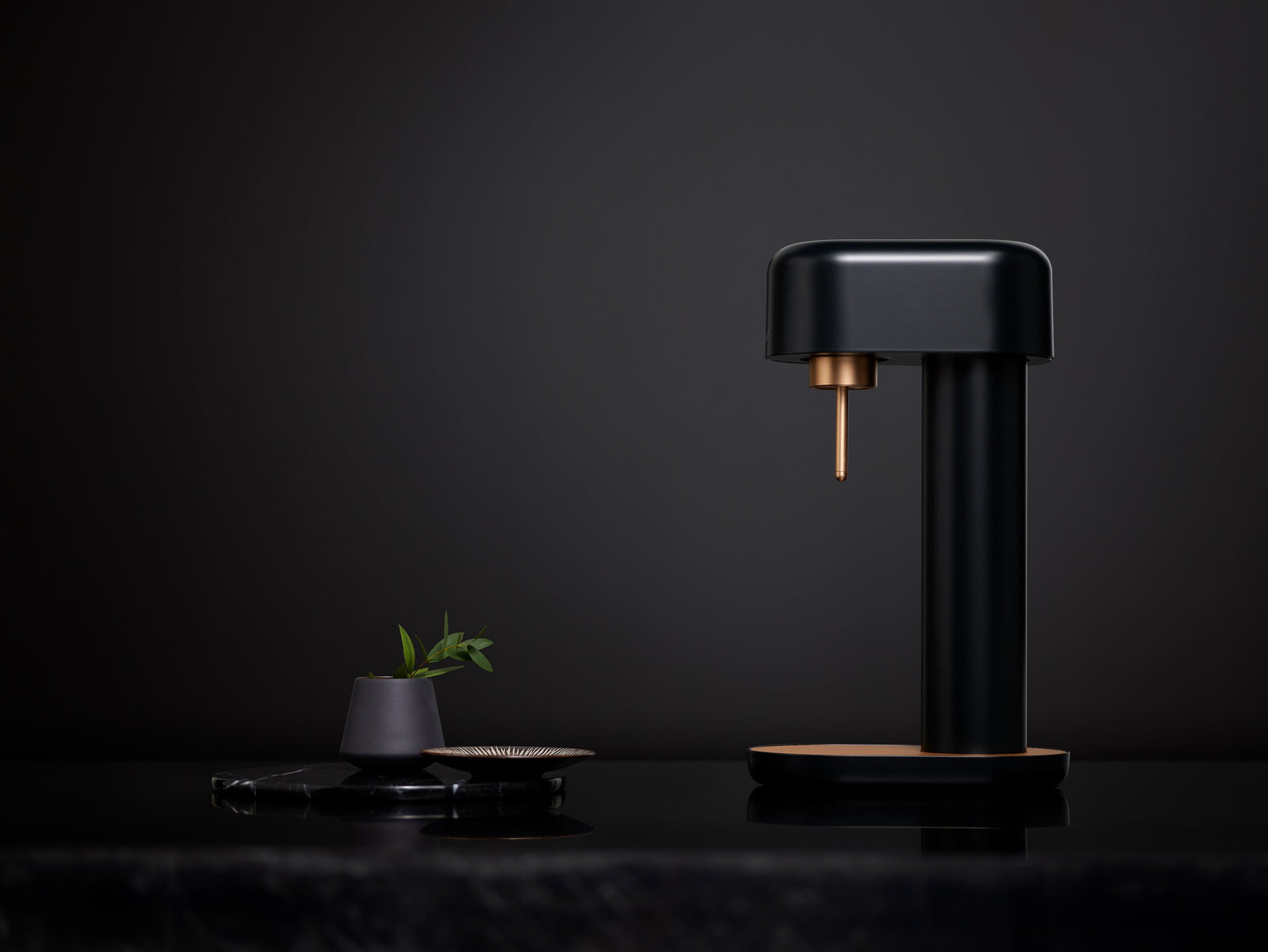 A black-copper sparkling water maker in an all-black studio setting